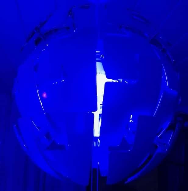 A close-up of an ion propulsion engine firing in a vacuum chamber, demonstrating the blue glow of the ionized gas being expelled. The image should highlight the intricate components of the engine and the controlled environment in which it operates.