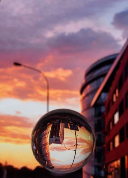 A close-up shot of a PhotoSharp Camera's lens, showcasing intricate glass elements and a professional finish, with a blurred background of a cityscape at golden hour.